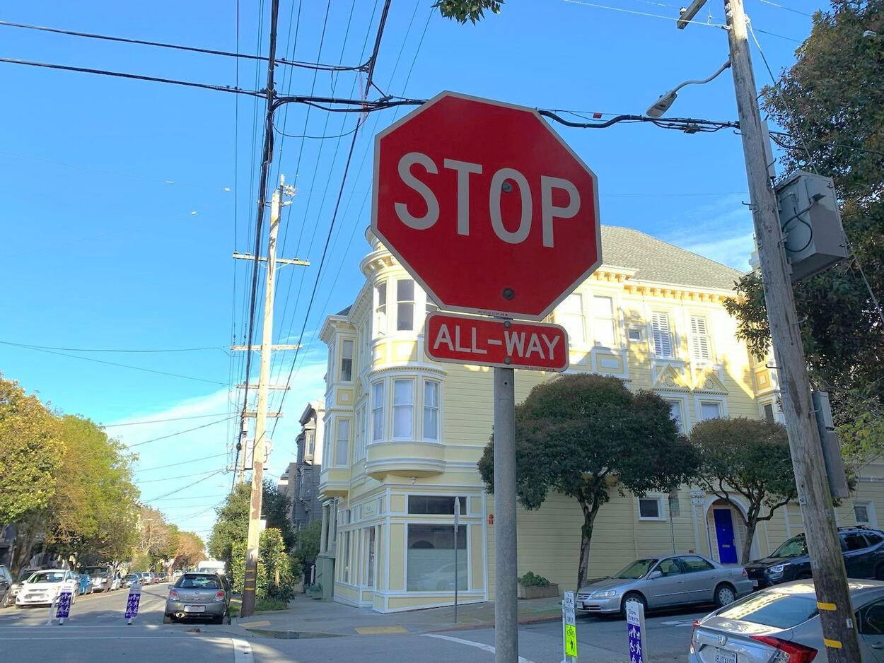 An all-way stop sign at an intersection of residential city streets.